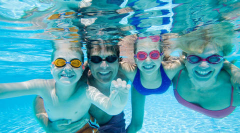 Family of 4 smiling in the pool underwater